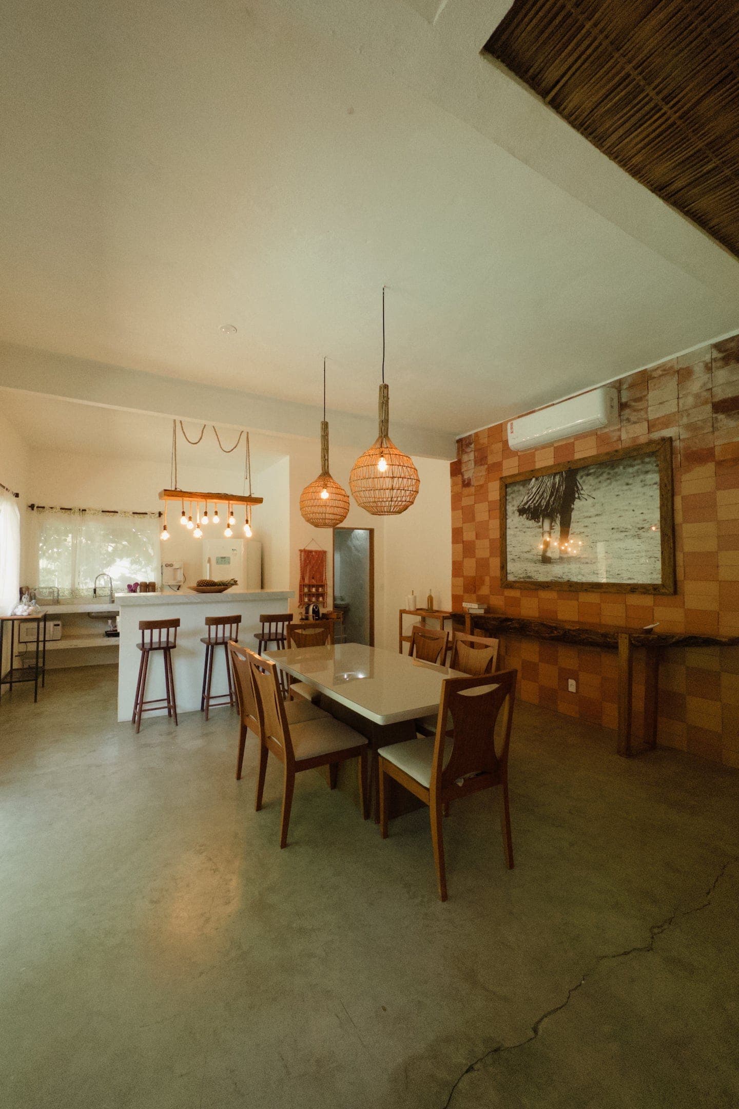 Sala de jantar com a cozinha ao fundo e luminárias de palha