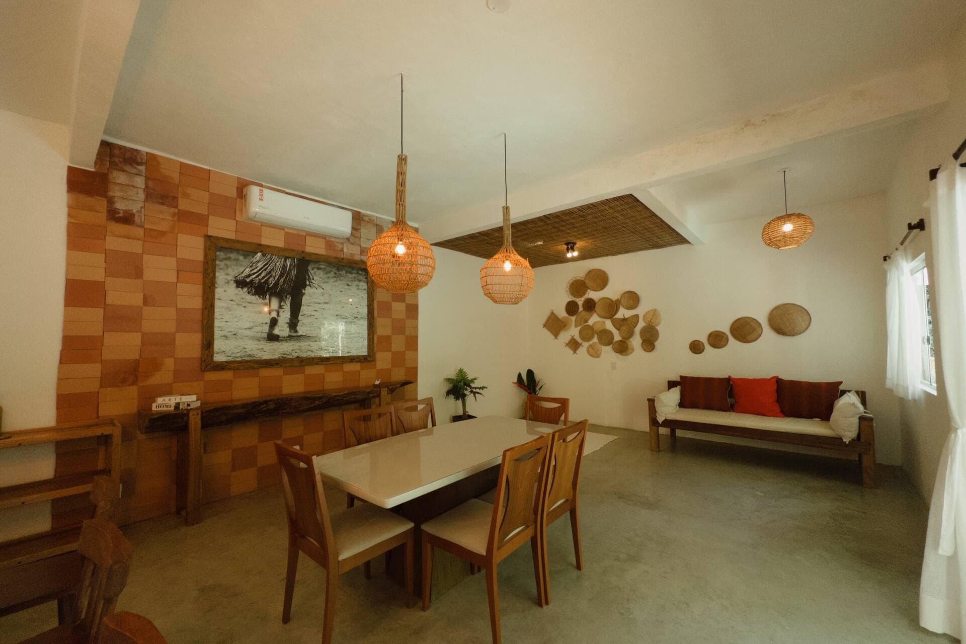 Sala de jantar e de estar integradas, com mesa de madeira, cestos na parede e painel em azulejo