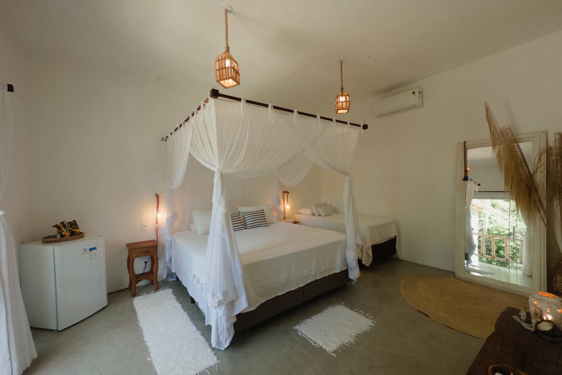Suíte com cama de dossel e mosquiteiro branco, frigobar e janela para o jardim
